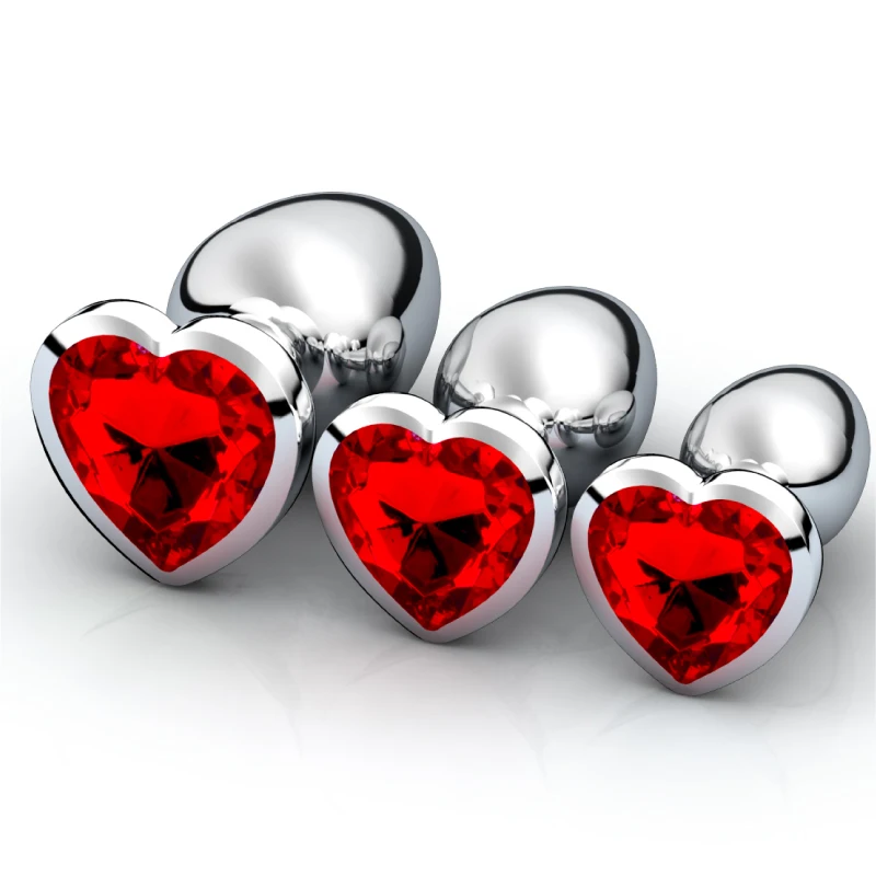 Three different sized stainless steel anal plugs with heart-shaped crystal bases arranged on a clean background.