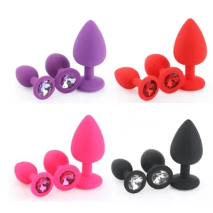 Three different sized silicone anal plugs with colorful diamond bases on a plain background.
