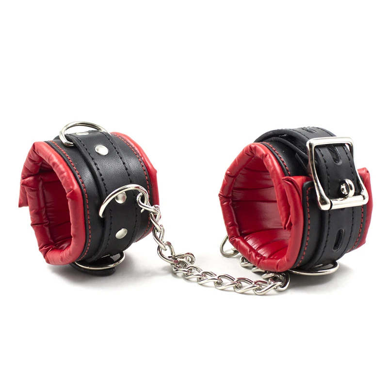 Close-up of black leather handcuffs and ankle cuffs with silver metal buckles and connecting chains for adult bondage play.