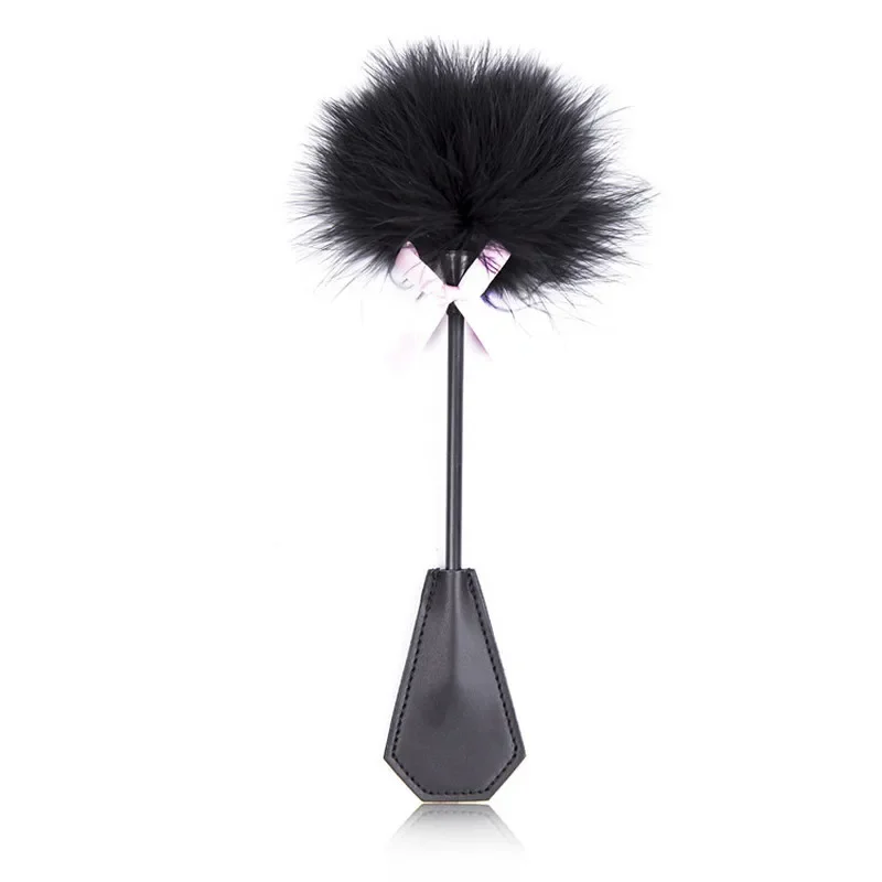 Close-up of a black leather spanking paddle and soft feather tickler for BDSM play.