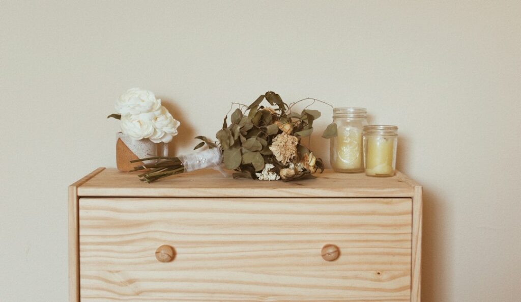 Minimal light wood dresser with dried flowers and glass jars representing cool dry private storage for personal items